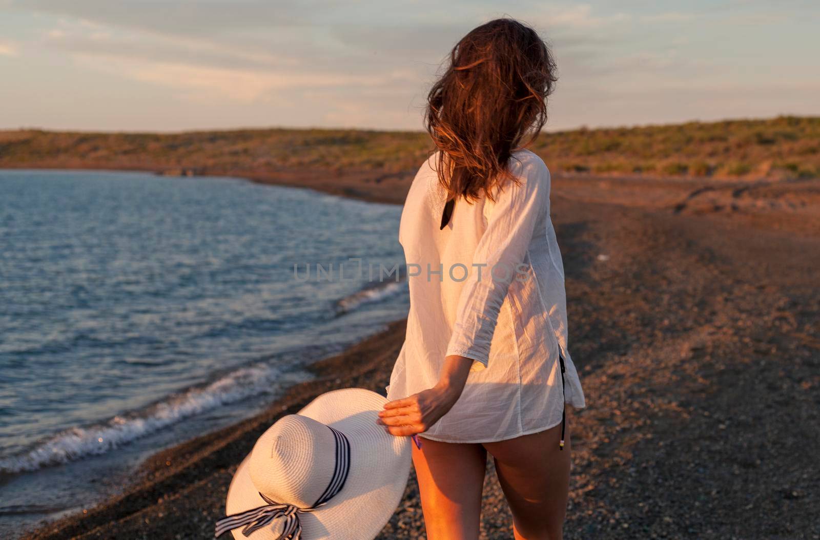 Woman walking on rocky beach with hat, rear view