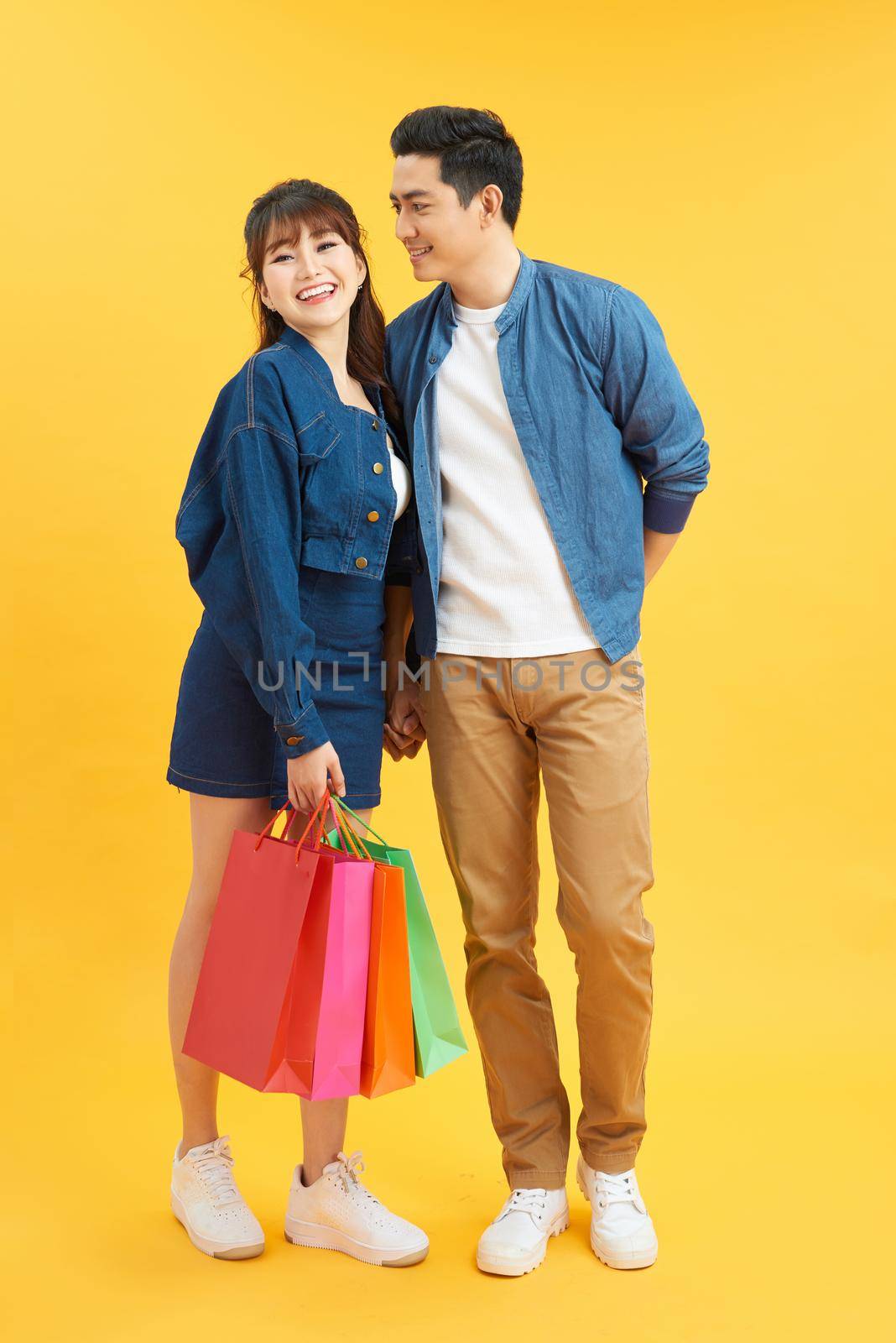 Happy young couple with shopping bags hugging and looking at each other isolated on yellow by makidotvn