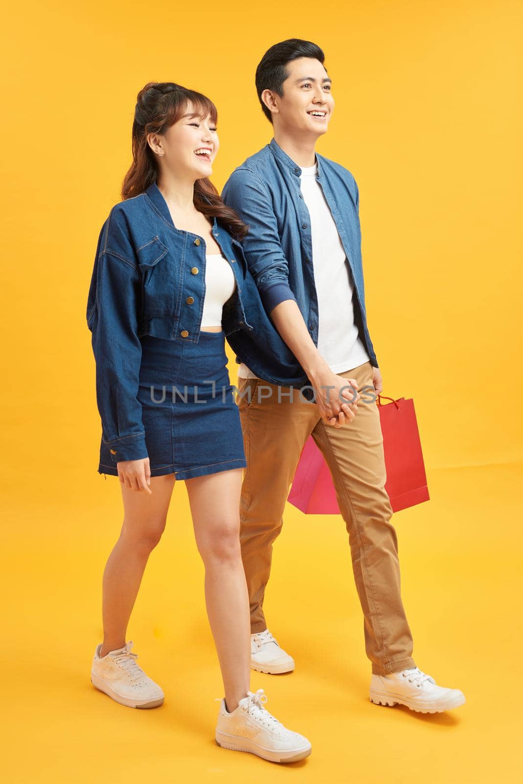 Full length portrait of a young couple walking with shopping bags isolated on yellow