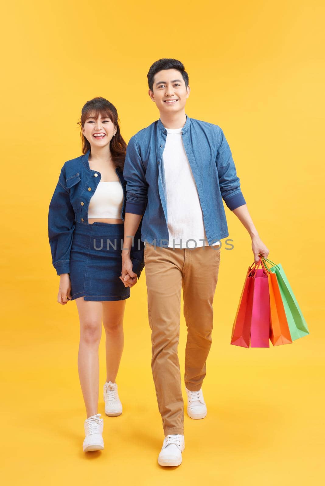 Beautiful young couple with shopping bags. Isolated on yellow background
