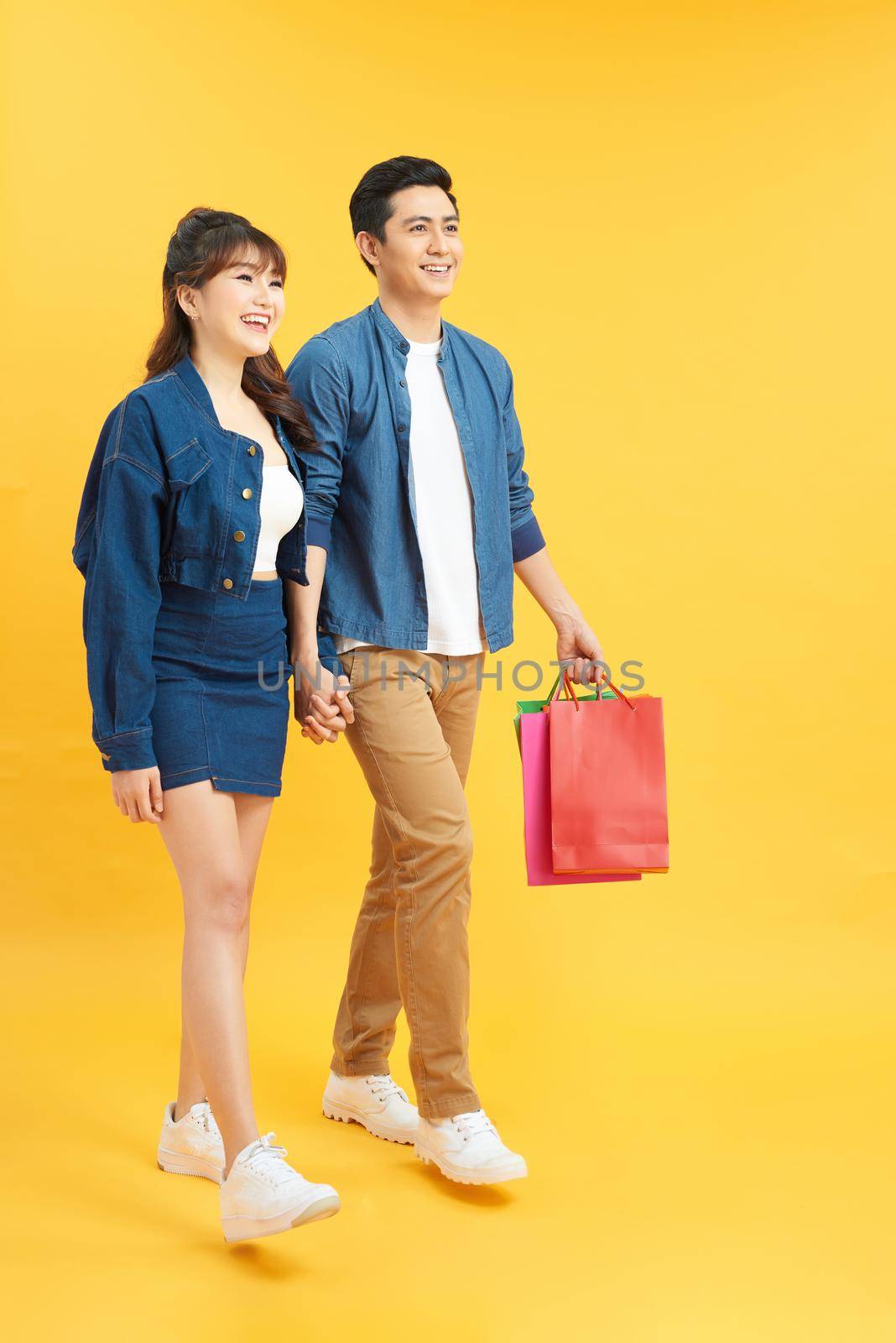 Happy young couple walking with shopping bags and looking at each other isolated on yellow by makidotvn