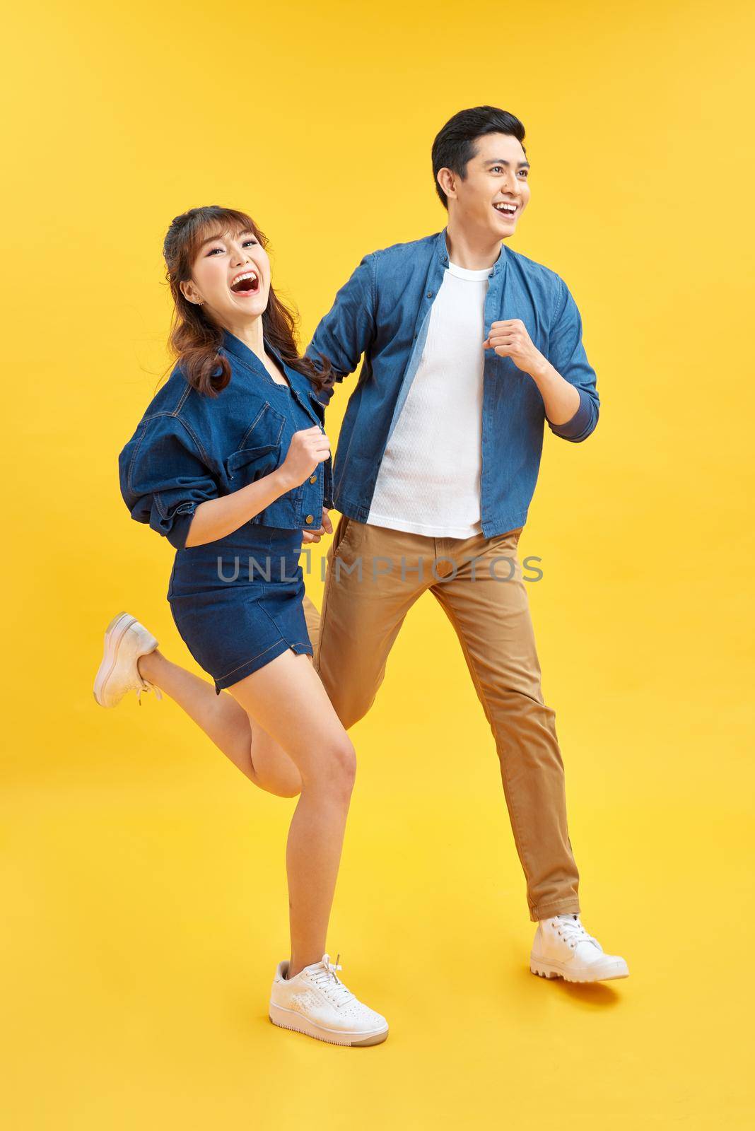 Attractive smiling young Asian couple being happy and amazed isolated on yellow studio background