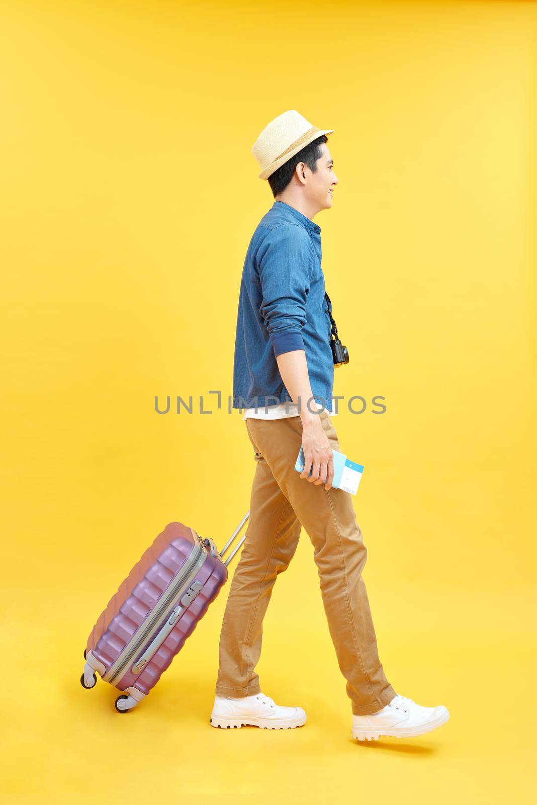 happy male tourist with travel bag and camera ready for trip, isolated on yellow by makidotvn