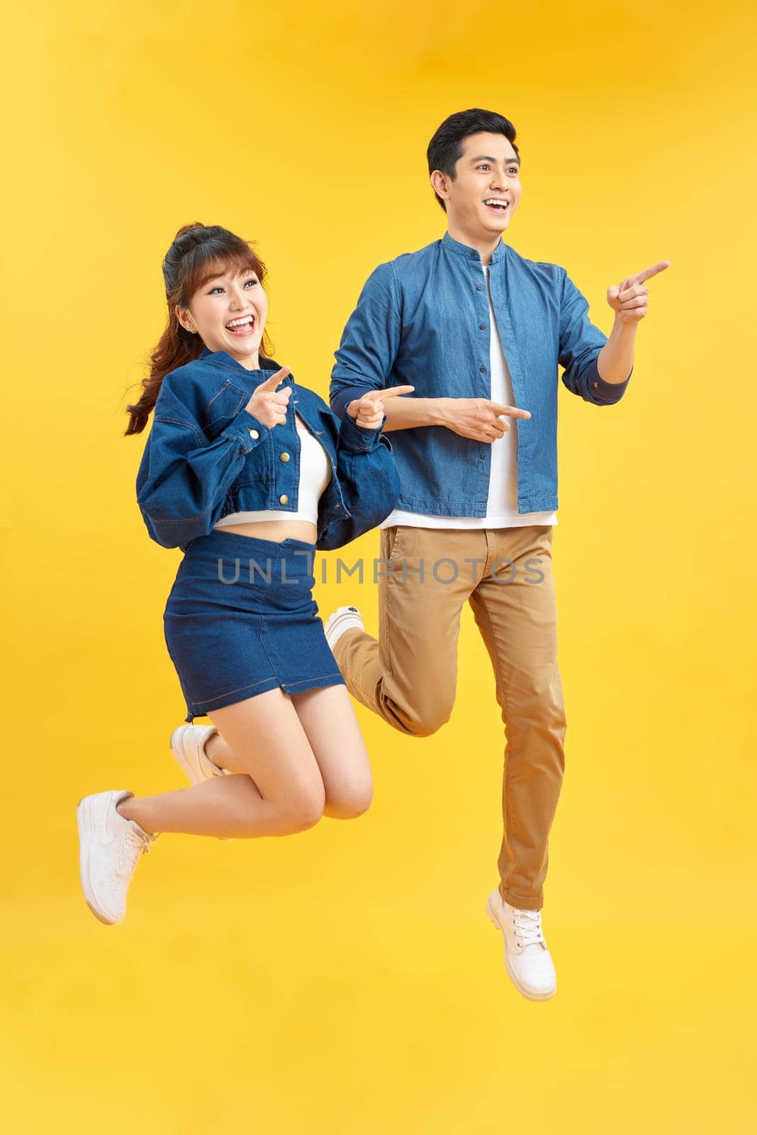 Portrait of funky couple jumping in air holding hands up enjoying time together isolated on yellow background