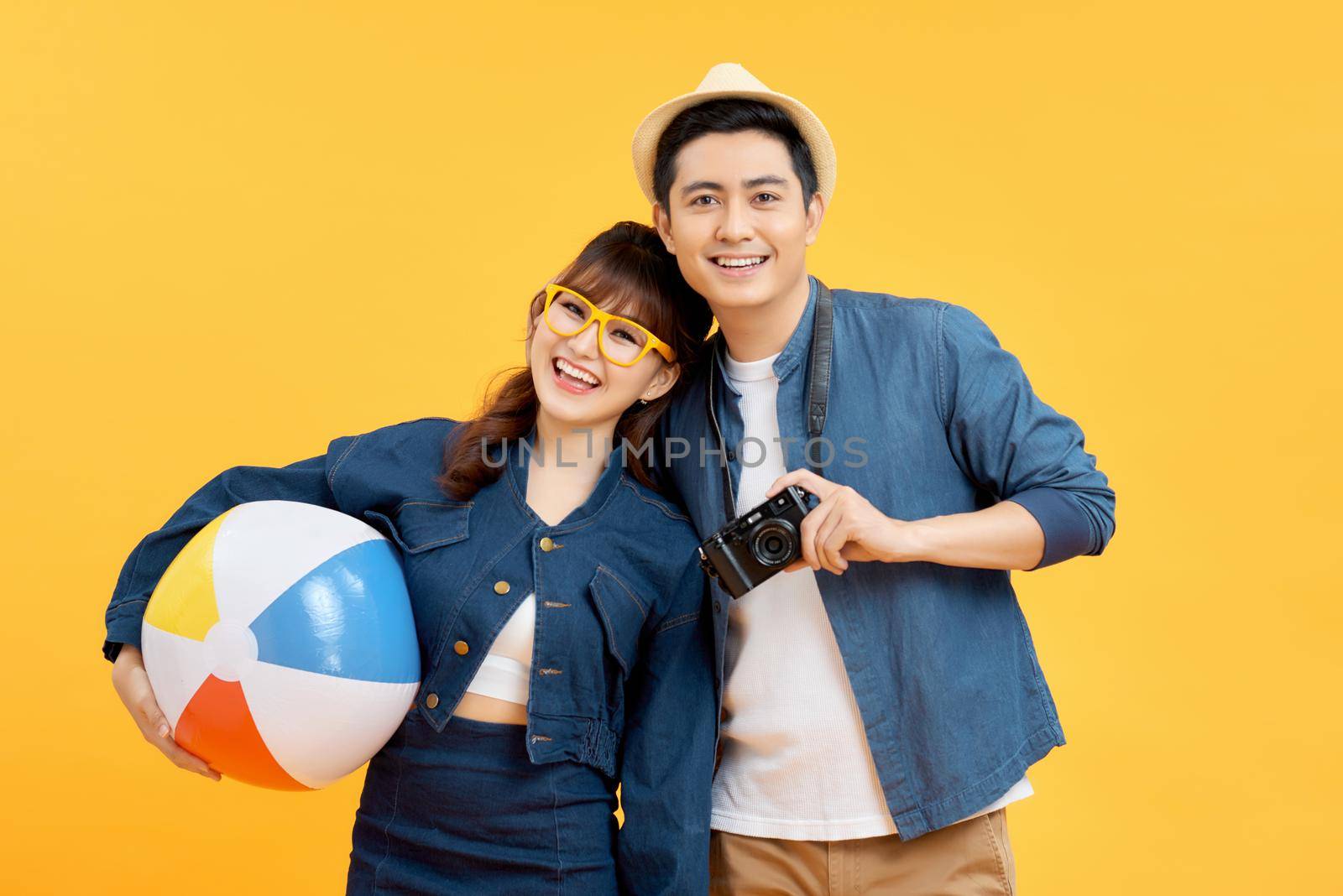Lovely Asian couple in summer casual clothes with beach accessories isolated on colorful yellow banner background with copy space