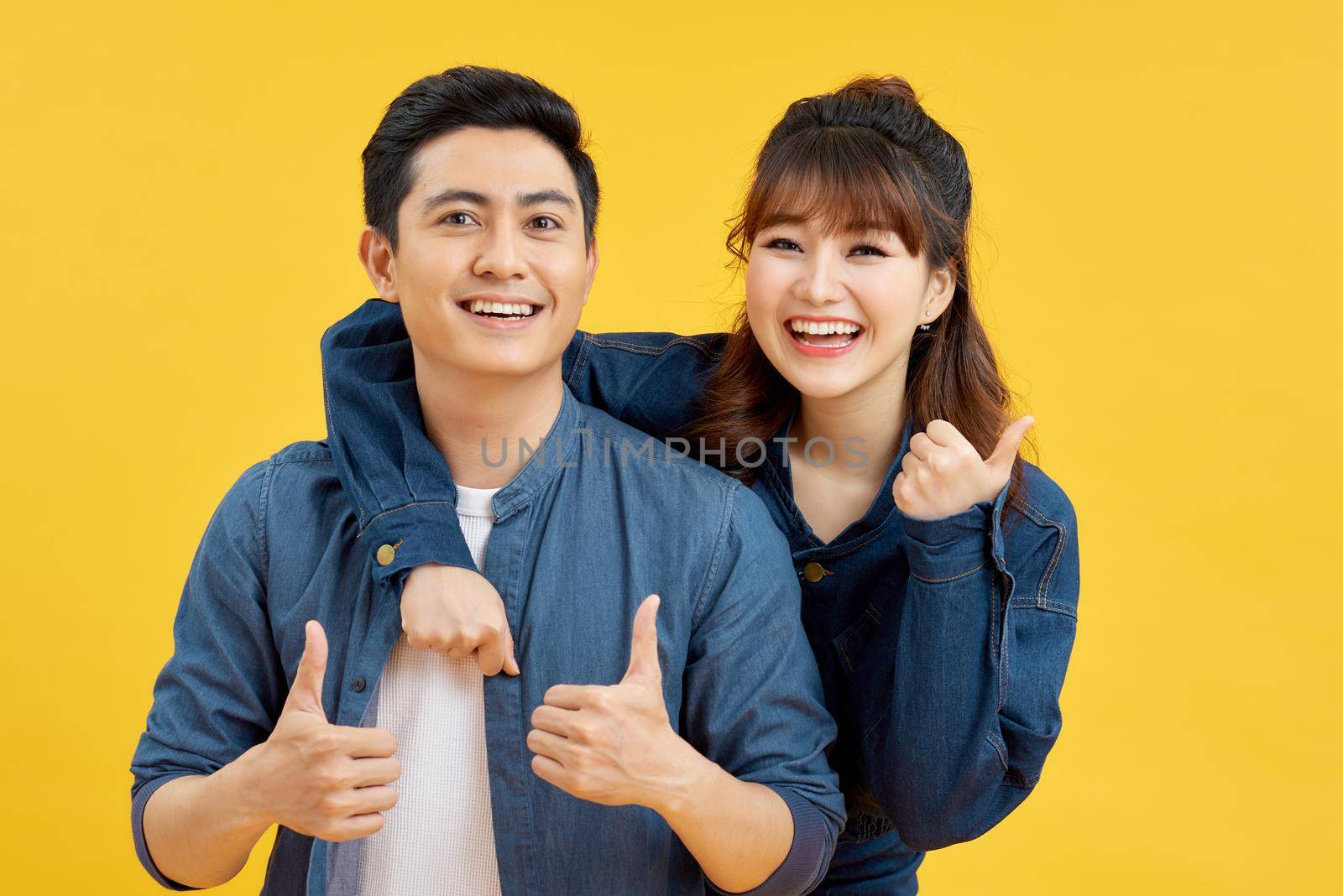 Attractive smiling young Asian couple being happy and amazed isolated on yellow studio background by makidotvn