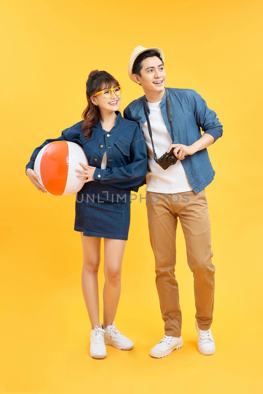 Playful Asian couple in summer casual clothes with beach accessories studio shot isolated on yellow background