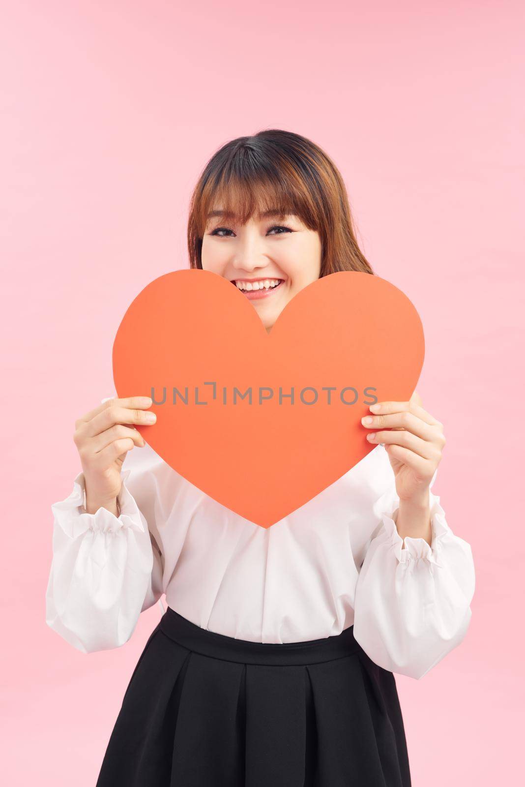 Cute asian woman holding red heart isolated on pink by makidotvn