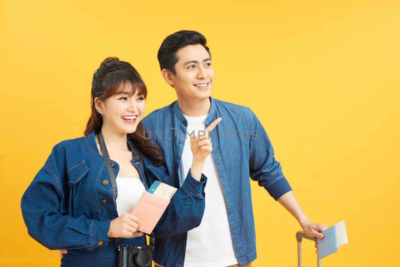 happy couple of tourists with suitcase luggages smiling showing pointing on yellow background isolation