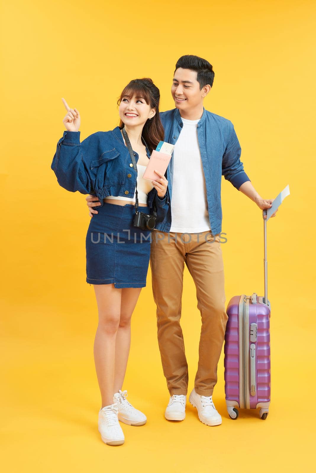 young travelling couple with suitcases pointing somewhere isolated on yellow by makidotvn