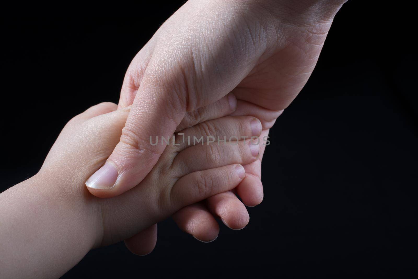 Adult and child hold hands in black background