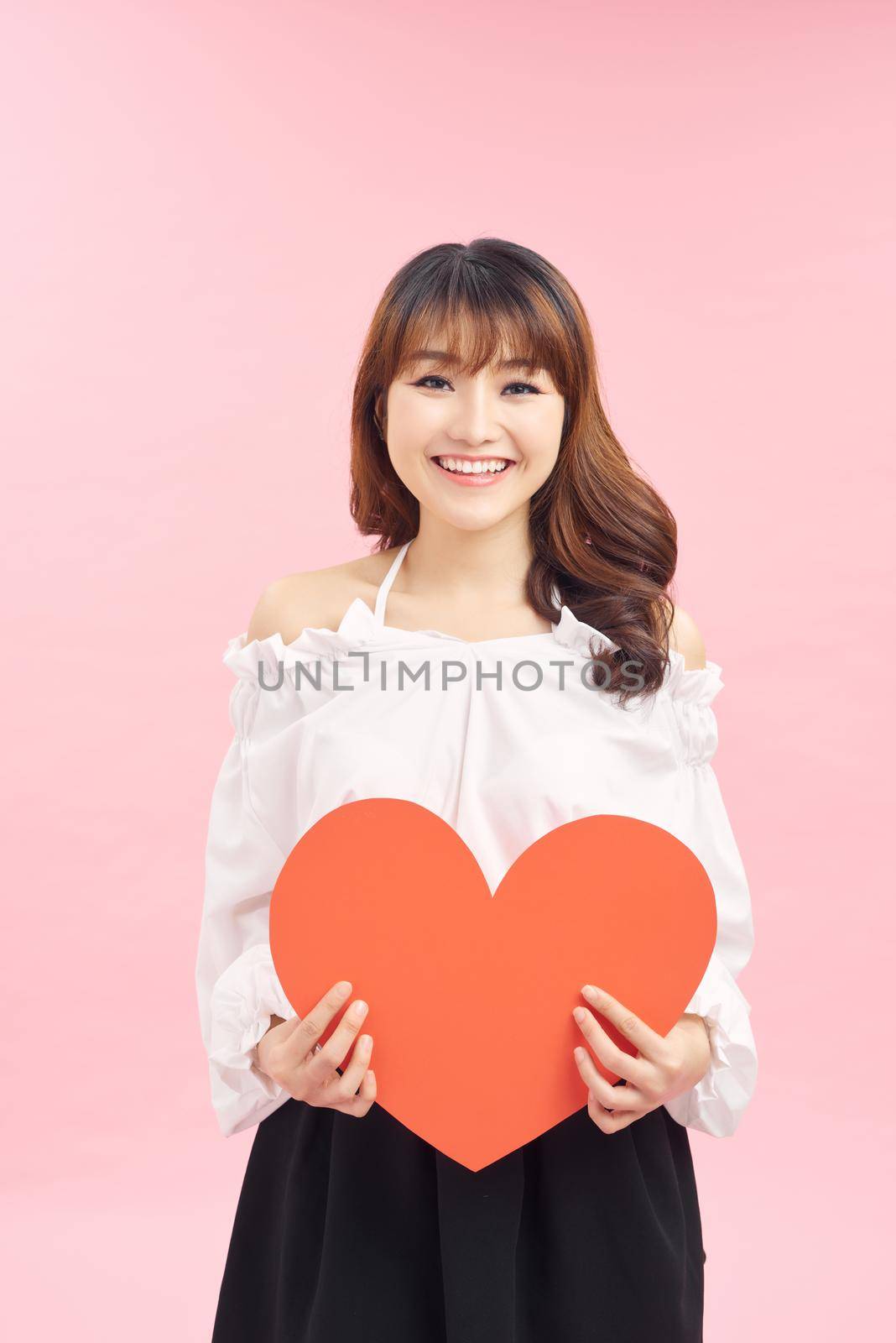 Beautiful asian girl with a card in the shape of a heart in her hands on a pink background. by makidotvn