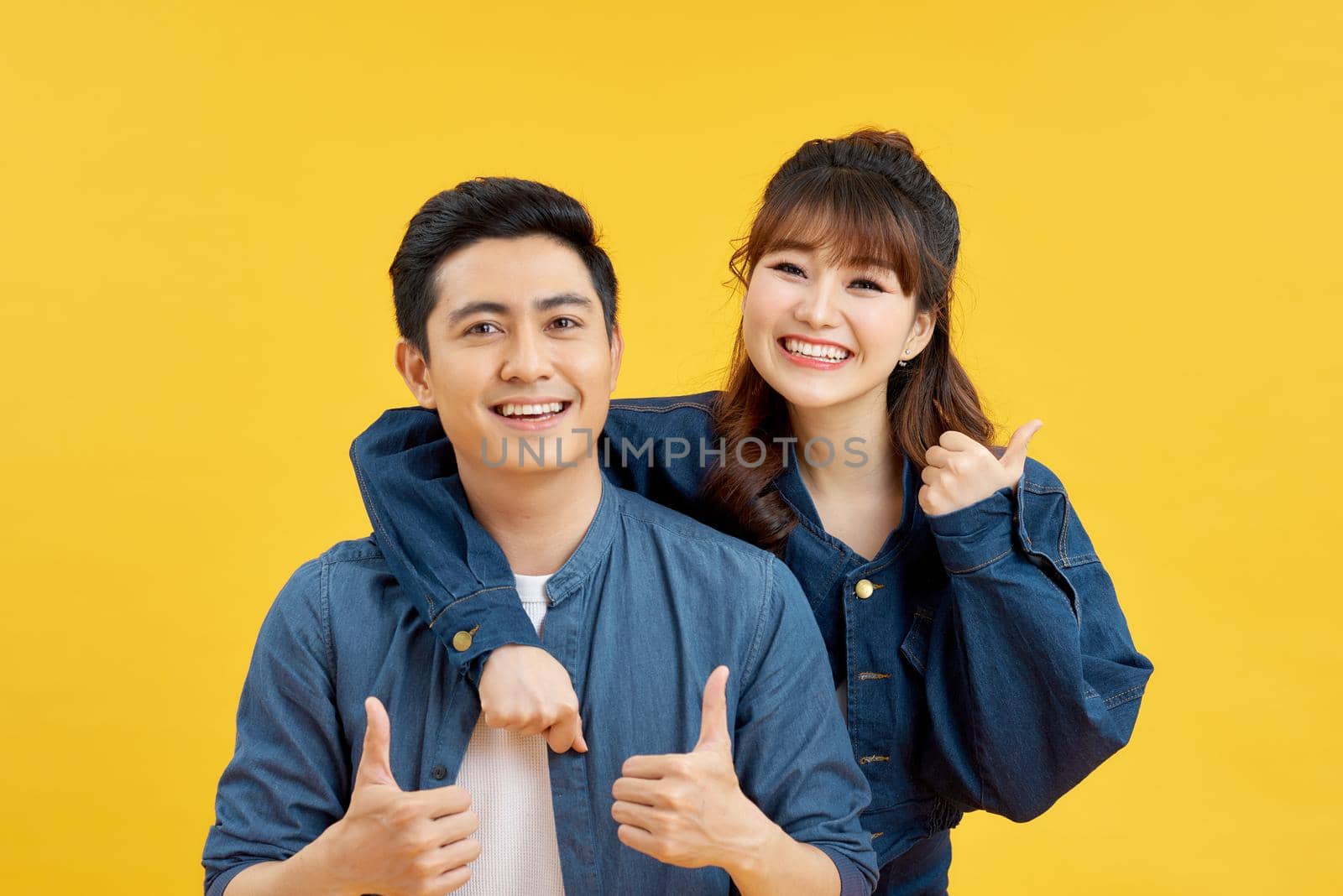Image of joyous couple showing thumbs up while man piggybacking joyful woman isolated over yellow background by makidotvn