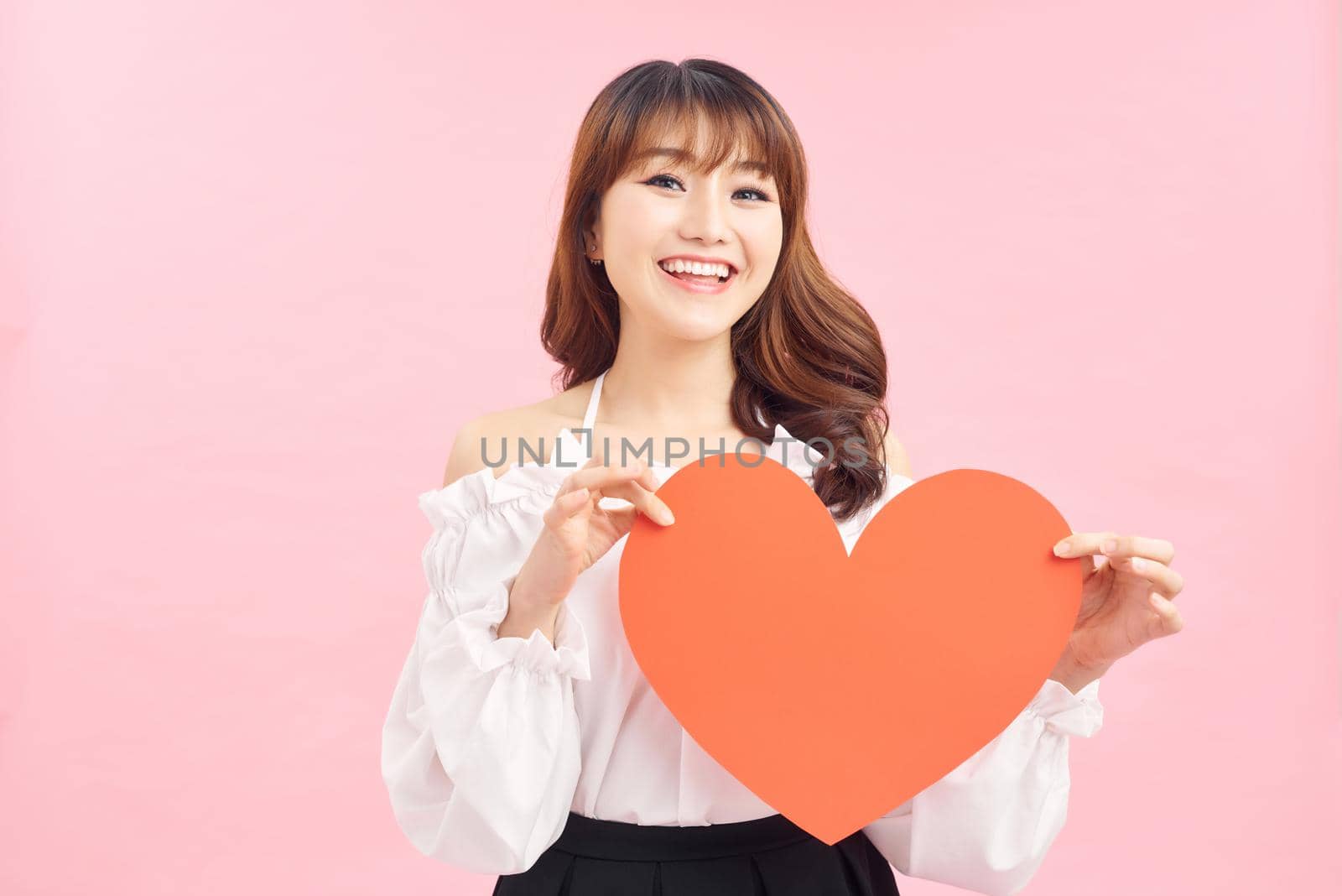 Image of gorgeous lady holding heart shaped paper against pink background by makidotvn