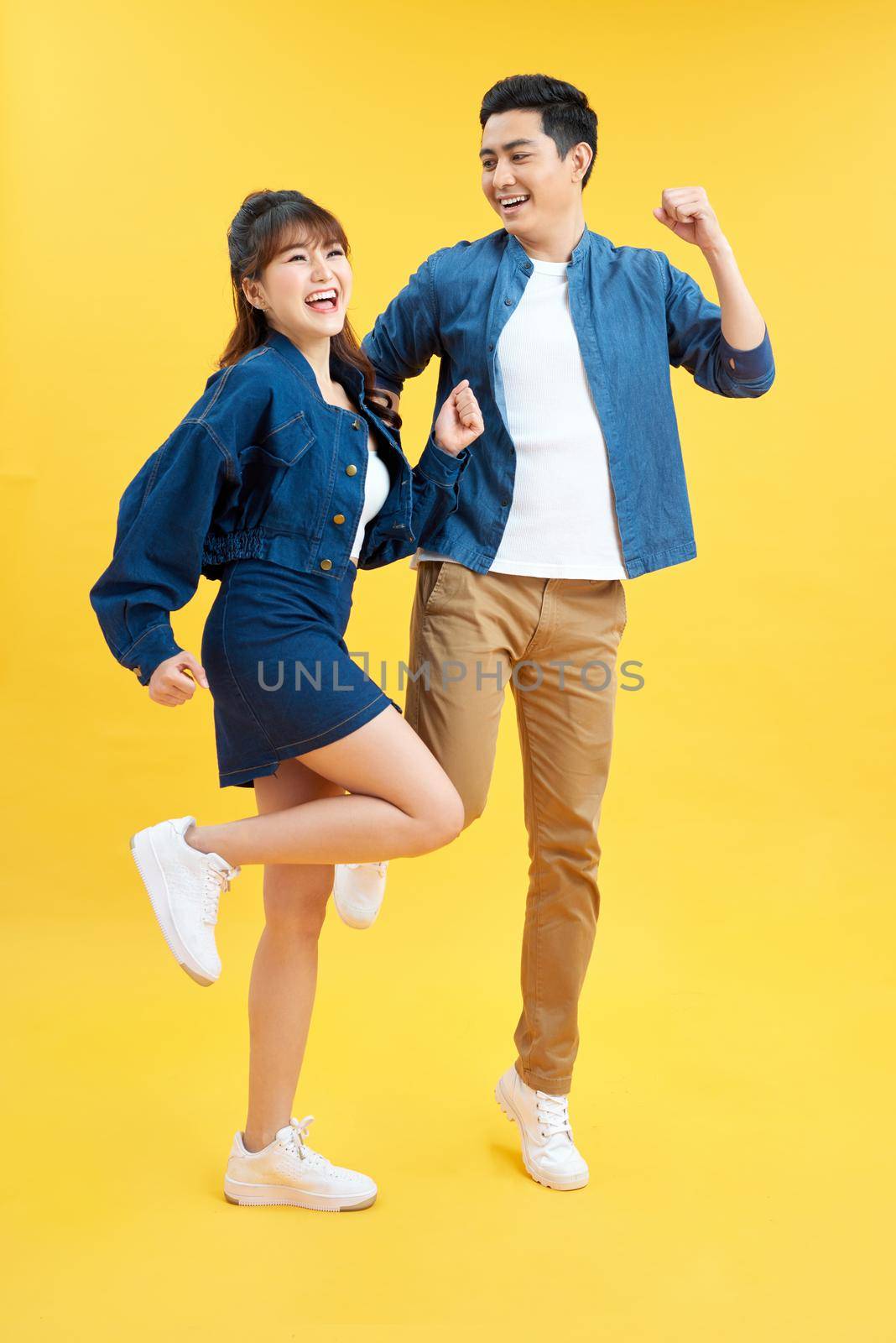 Full length body size photo funky she her he him his pair jumping high raised fists yell scream shout loud wear casual jeans denim white t-shirts isolated yellow background by makidotvn
