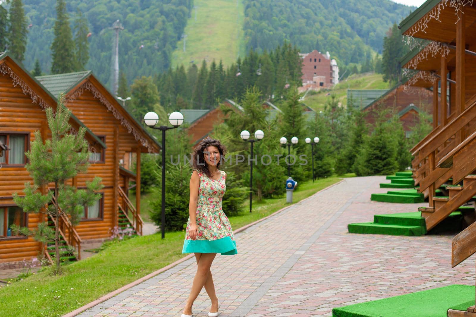A beautiful slim girl posing next to mountain ski resort in the summer day.