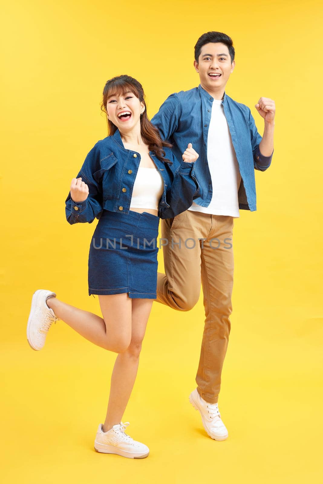 Full length portrait of amazed couple man and woman in basic t-shirts rejoicing while clenching fists isolated over yellow background