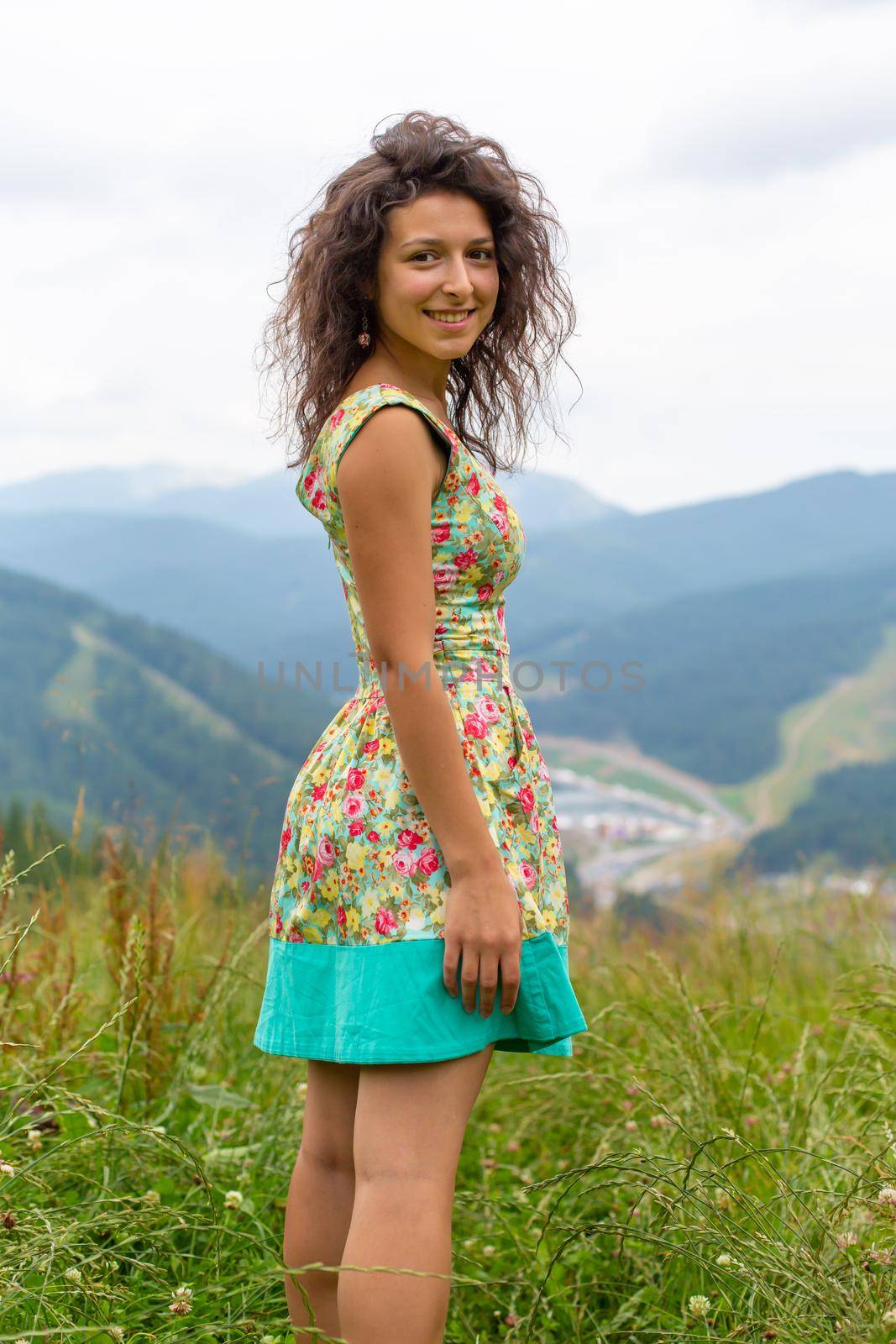 Happy gorgeous girl enjoy mountain view stay in summer dress on the hill with breathtaking mountain landscape.