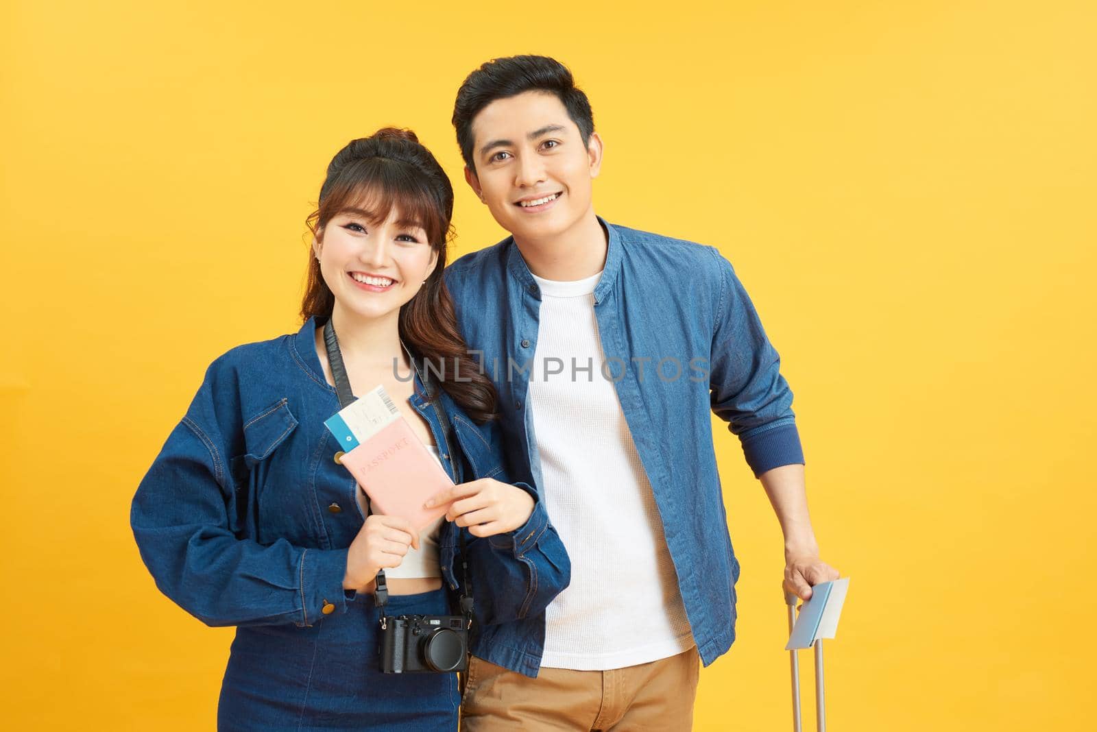 Traveler asian couple with backpack and suitcase standing isolated over yellow background