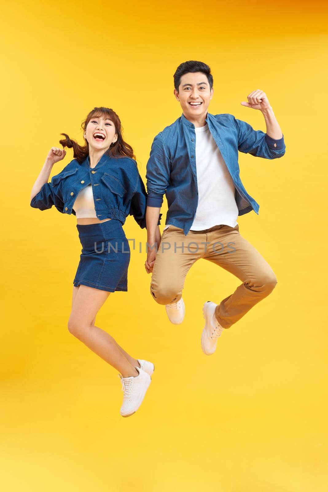 Full length portrait of amazed couple man and woman in basic t-shirts rejoicing while clenching fists isolated over yellow background by makidotvn