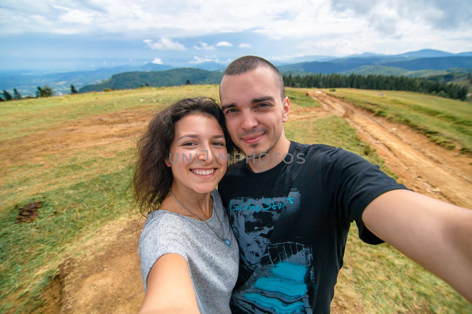 Young couple hugs and take selfie with amazing mountain landscape background.