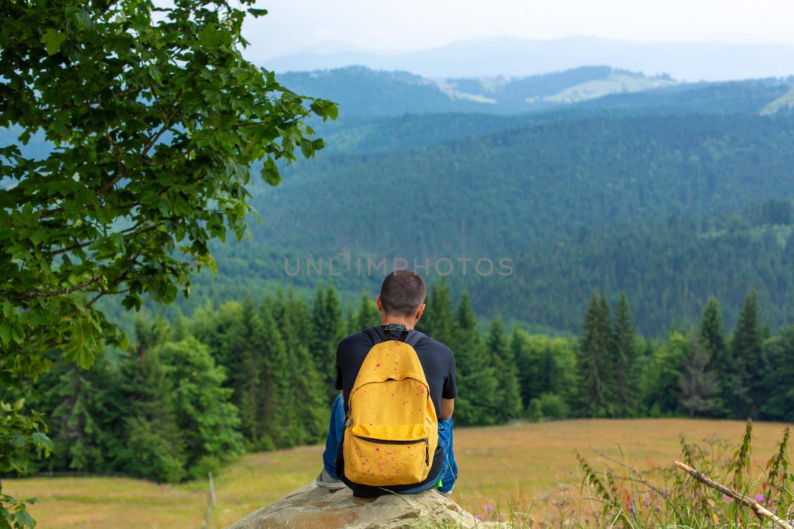 Alone guy sitting on cliff and enjoy peaceful green mountains landscape. Peace of mind and relax.