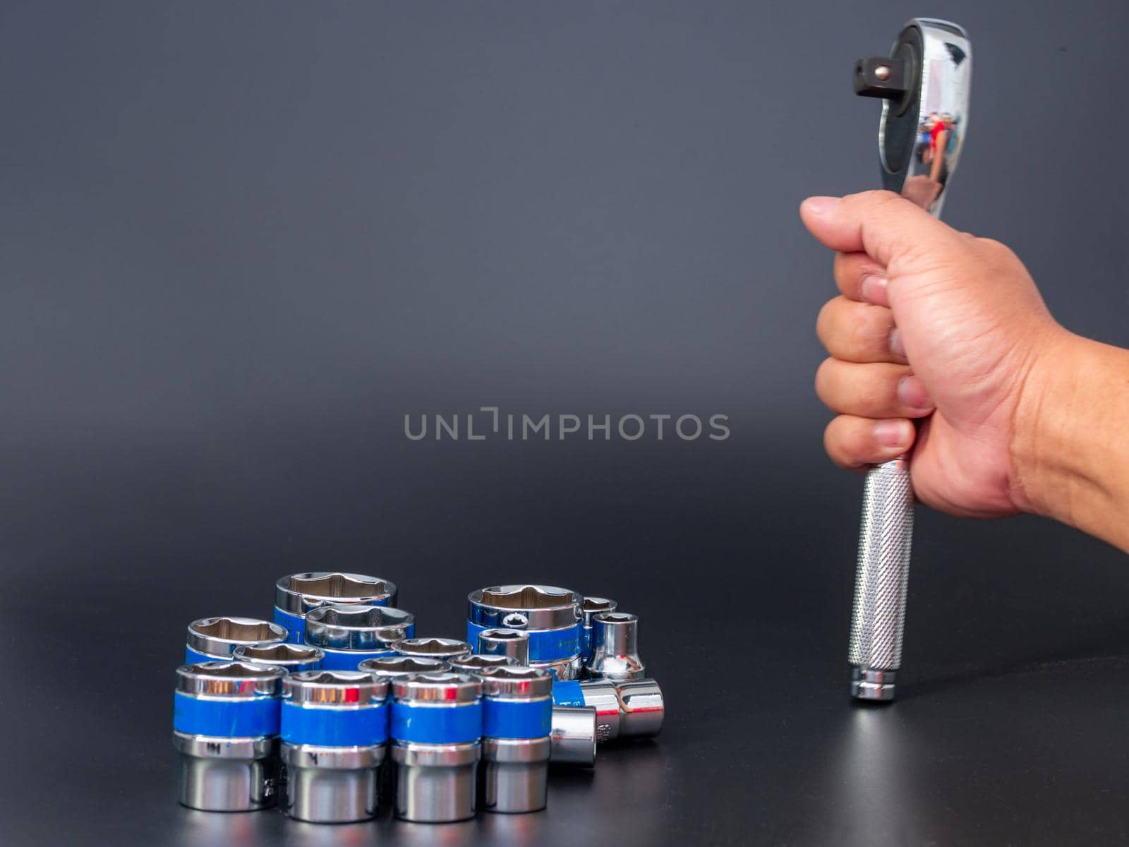 block wrench set and the hand of a man holding a ratchet wrench on a black background. by Unimages2527