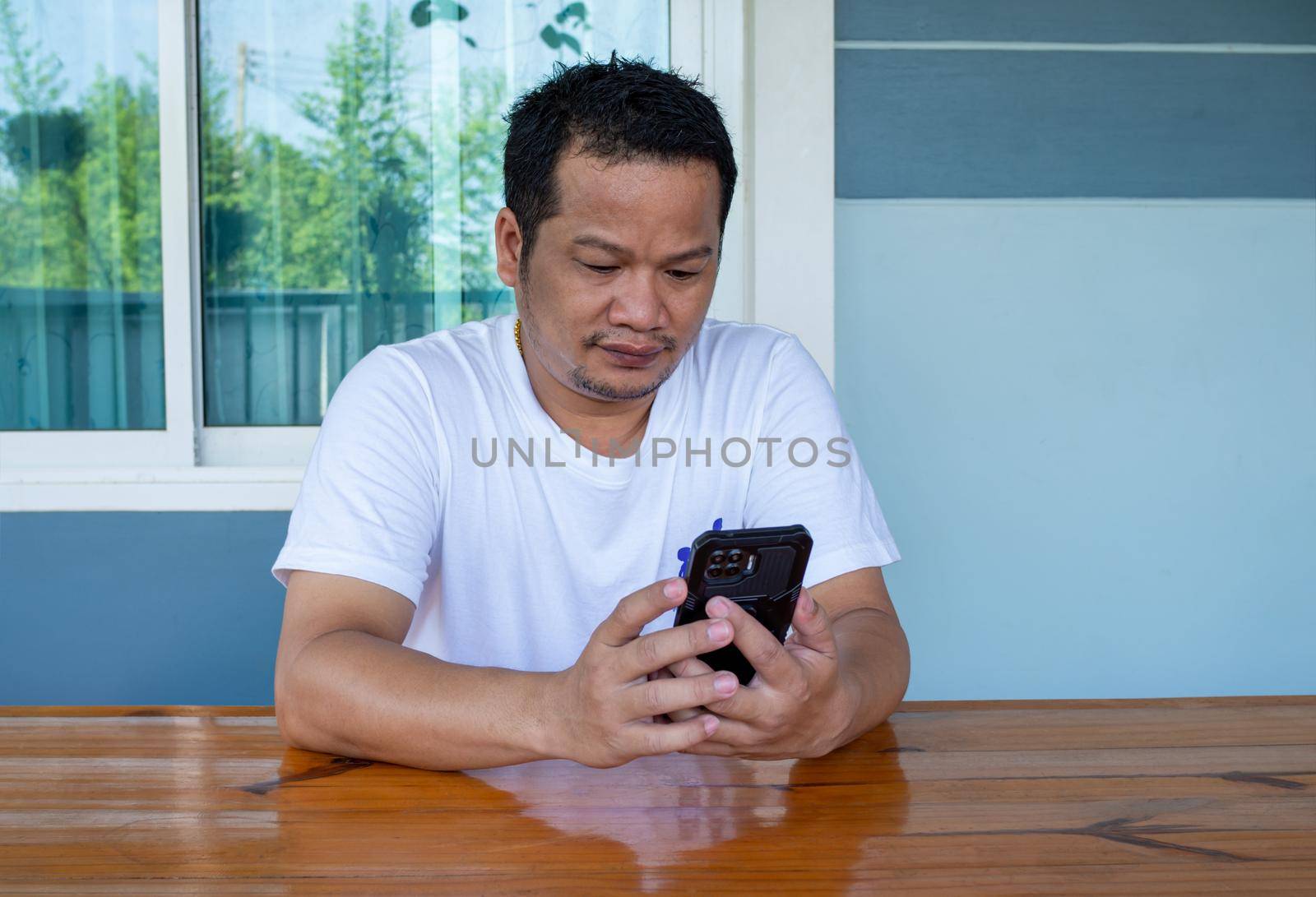 Asian man wearing white shirt using the phone on a wooden table by Unimages2527