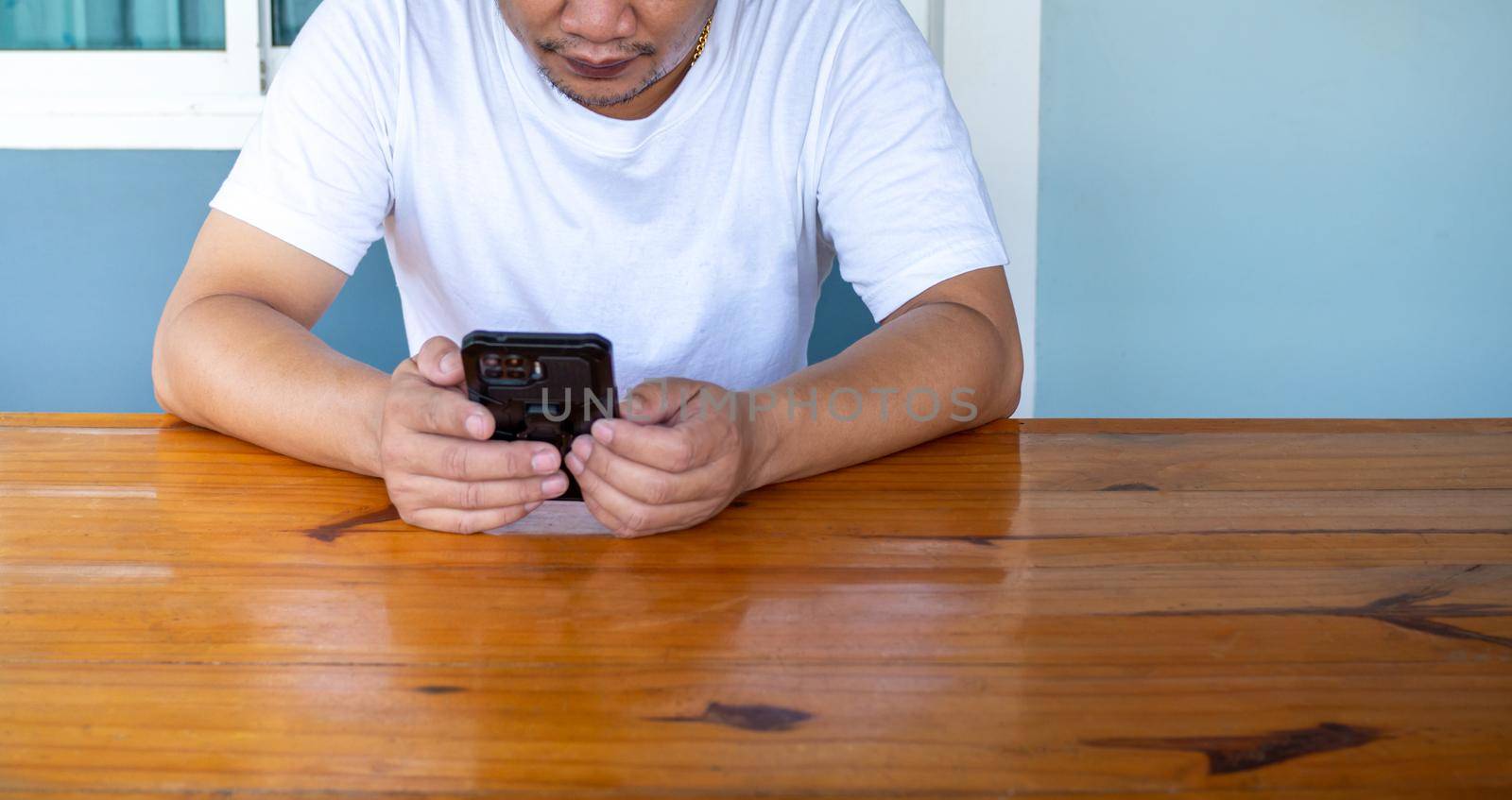 Asian man wearing white shirt using the phone on a wooden table