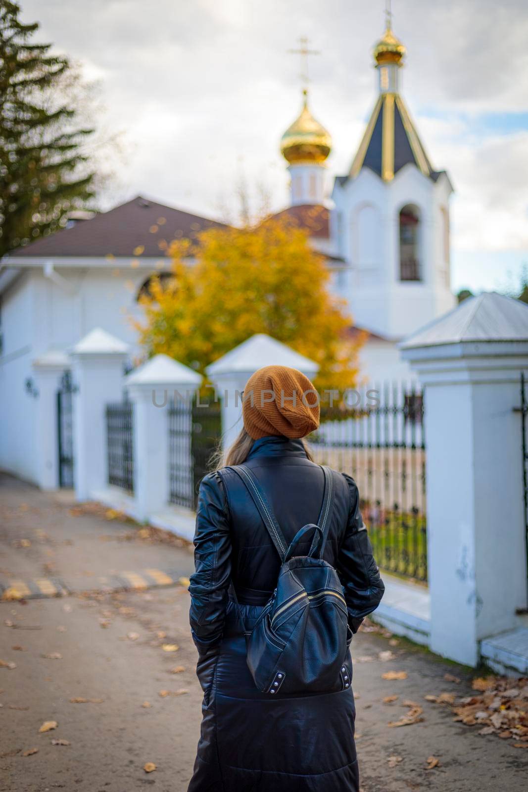 Near the church, a young girl walks in thought. Autumn time, yellow leaves