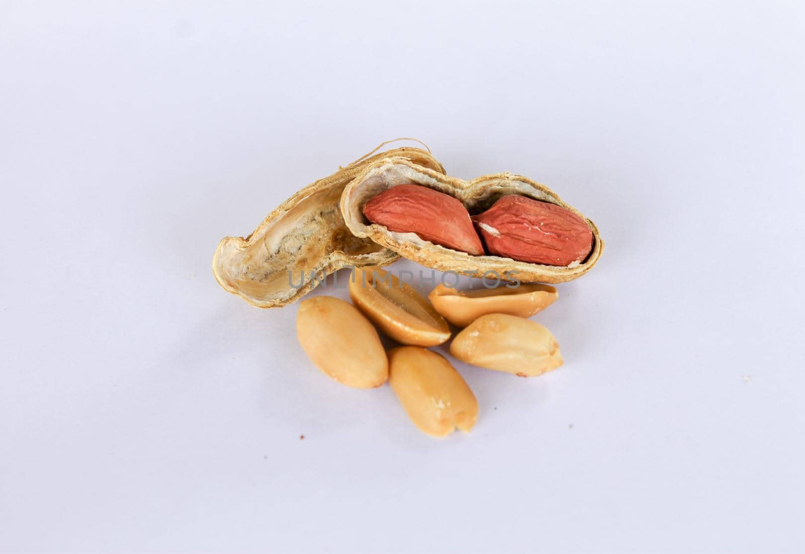 Peanuts piled up separately on a white background . One has been peeled off to reveal a red seed inside. There are two seeds that have been carved apart in front. by pichai25