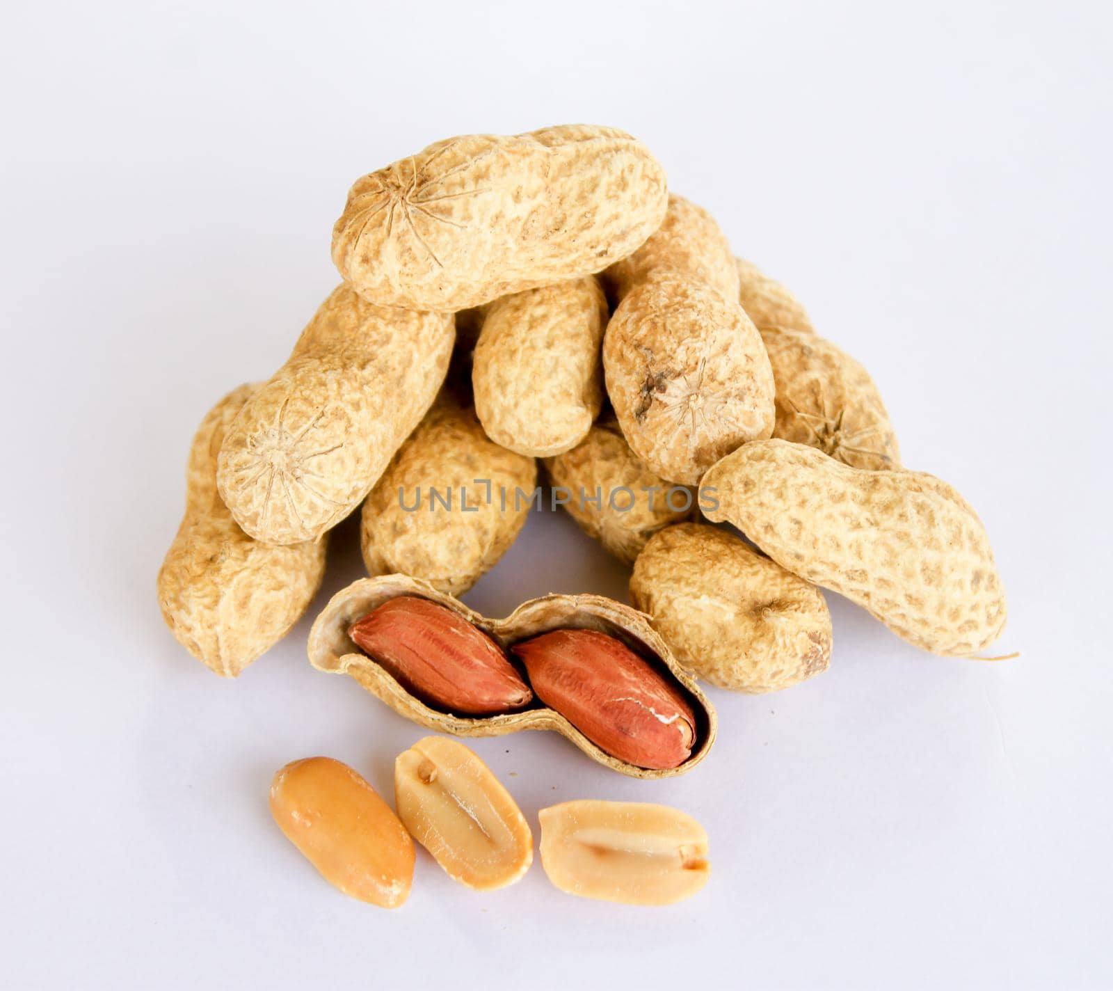 Peanuts stacked separately on a white background . Two kernels have already been removed. One of the peanuts unpacked reveals a red seed on the side. The seeds are separated from each other in the front.