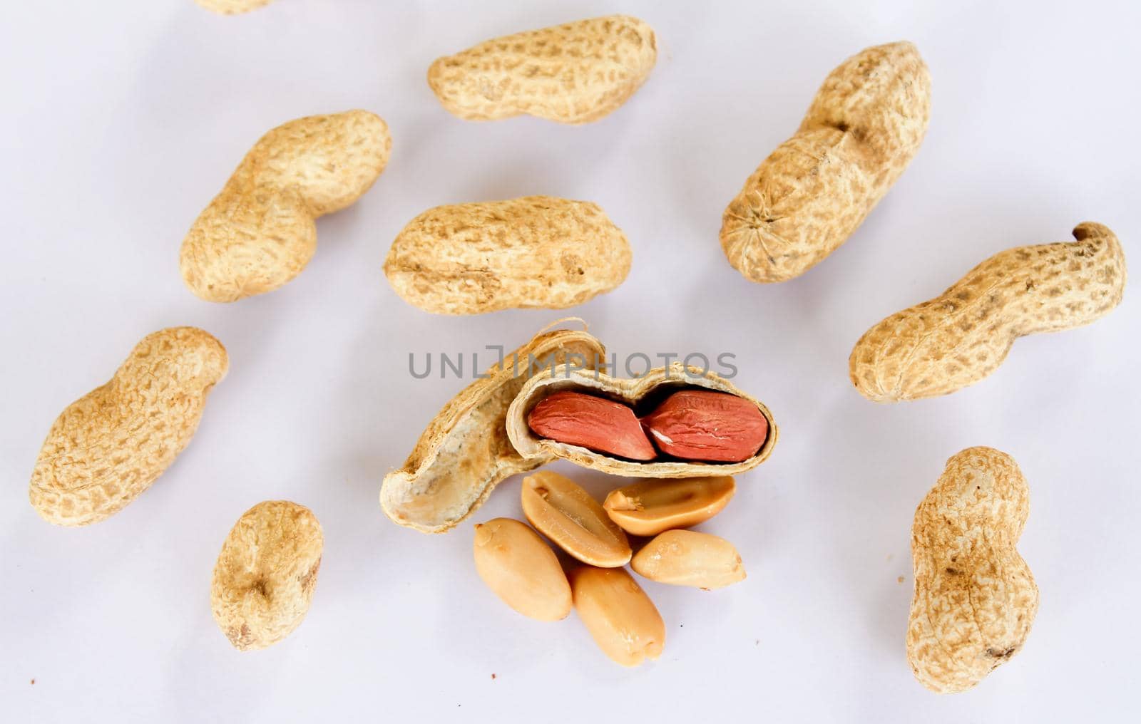 Peanuts scattered on a white background. One was opened to reveal a red seed inside. by pichai25