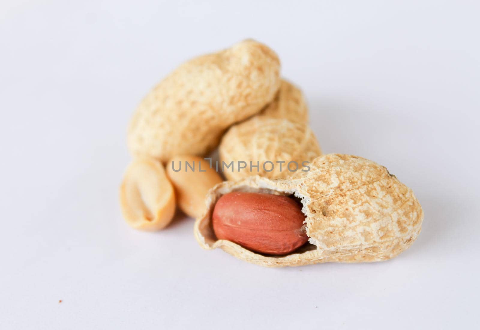 Peanuts are on a white background. One was peeled to reveal a red seed inside. close-up photo of peanuts