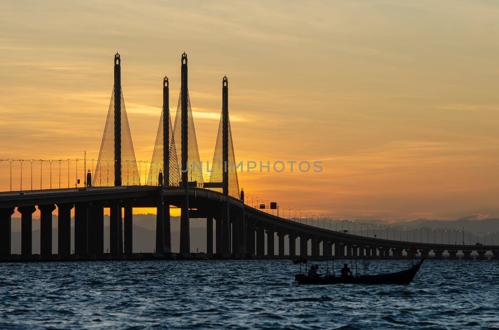 Silhouette fishing boat near Penang Second Bridge during sunrise.