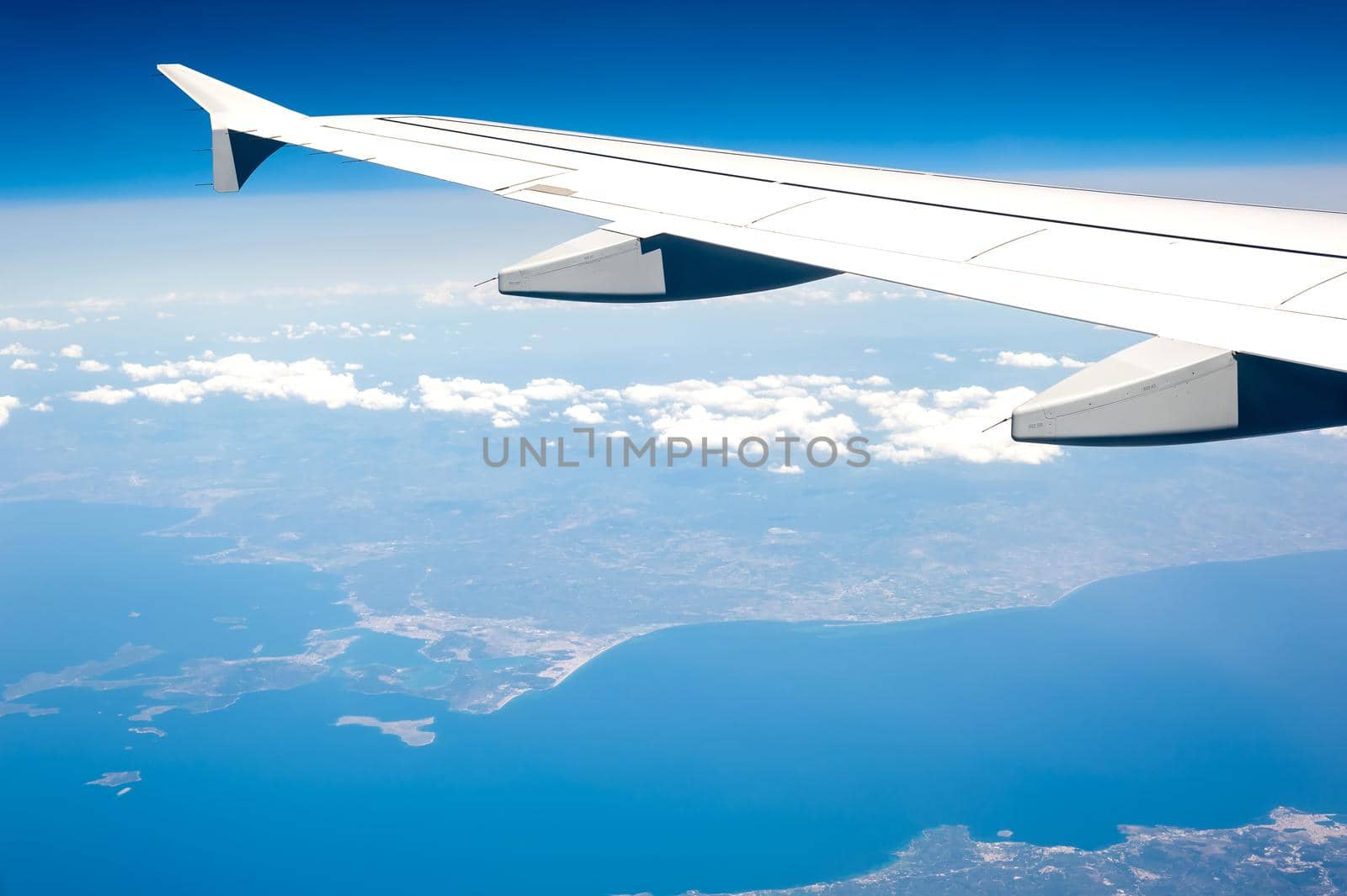 View from airborne airplane window at cloudy sky and Mediterranean coastline from high altitude. by Qba