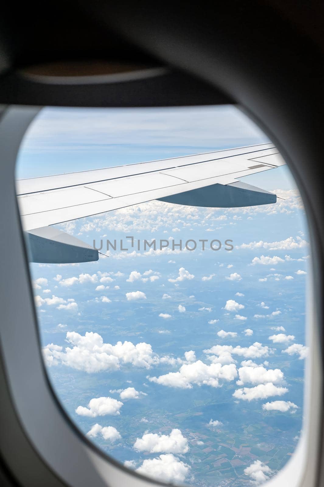 View from airborne airplane window at cloudy sky and land with fields from high altitude.