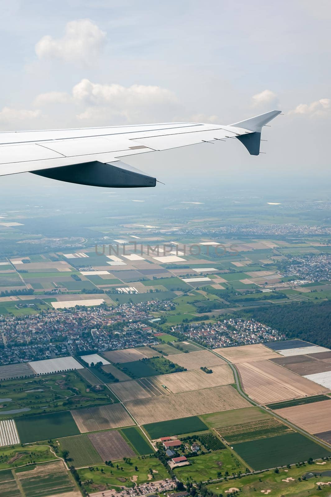 View from airborne airplane window at cloudy sky and land with fields from high altitude.