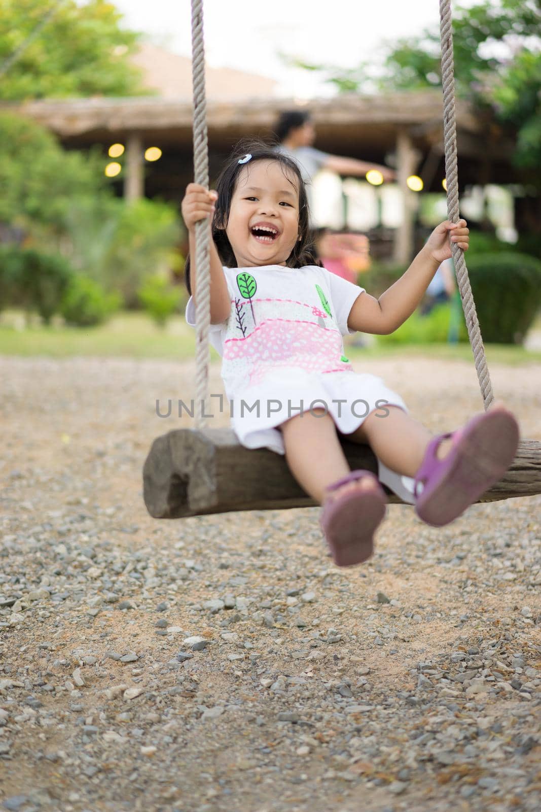 Little girl in white dress sitting on a swing in the park by domonite