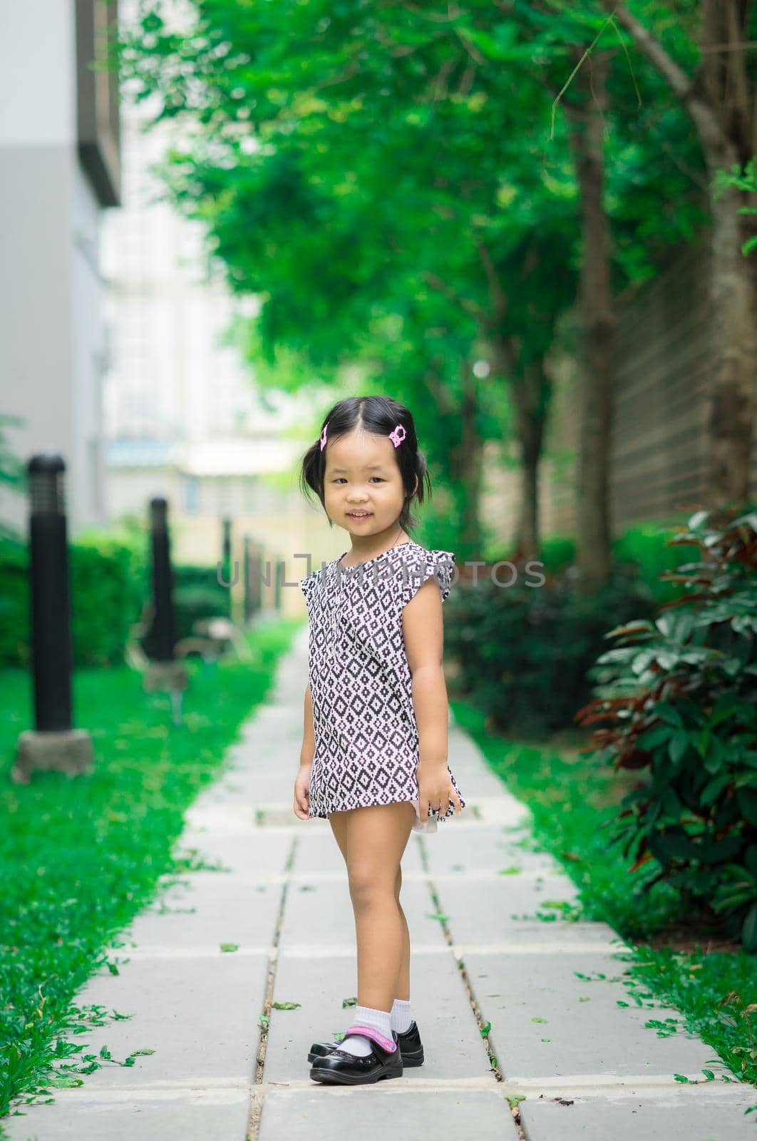 Portrait of happy asian little girl in dress standing on footpath in the park by domonite