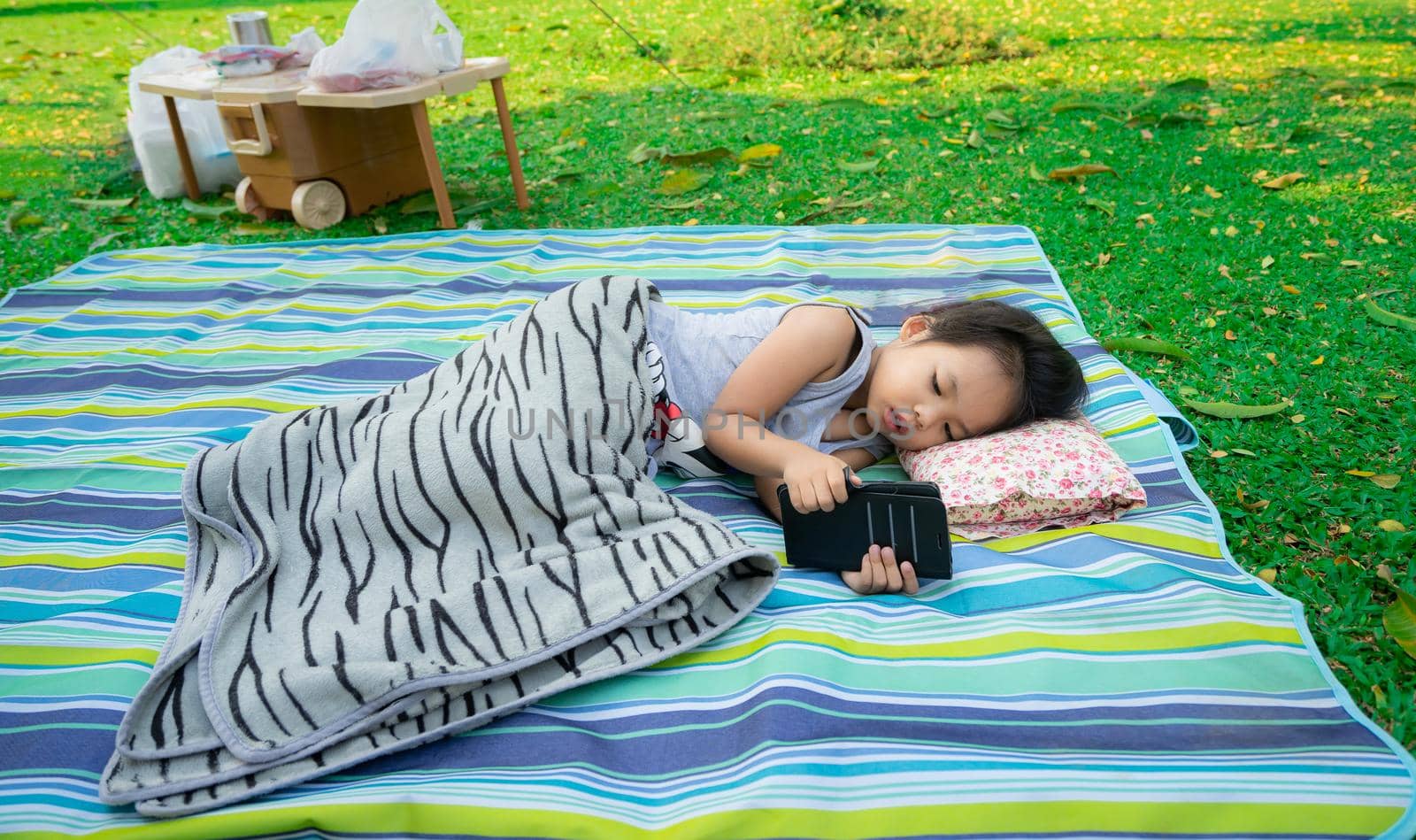 little girl looking at mobile phone while lying in the park by domonite
