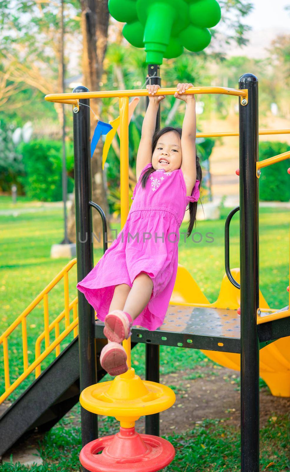 Cute asian little girl hanging on a horizontal bar while playing in the playground by domonite
