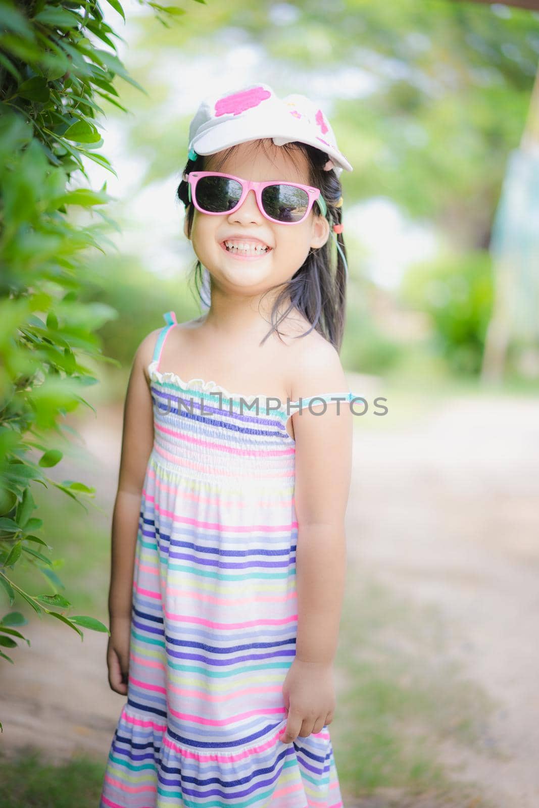 portrait of cute asian little girl wear sunglasses and hat in the park by domonite