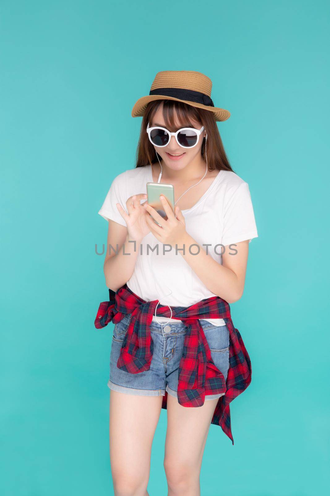 Beautiful portrait young asian woman listening music on phone with earphone isolated on blue background, asia girl using smartphone excited and fun with relax in travel summer trip concept. by nnudoo