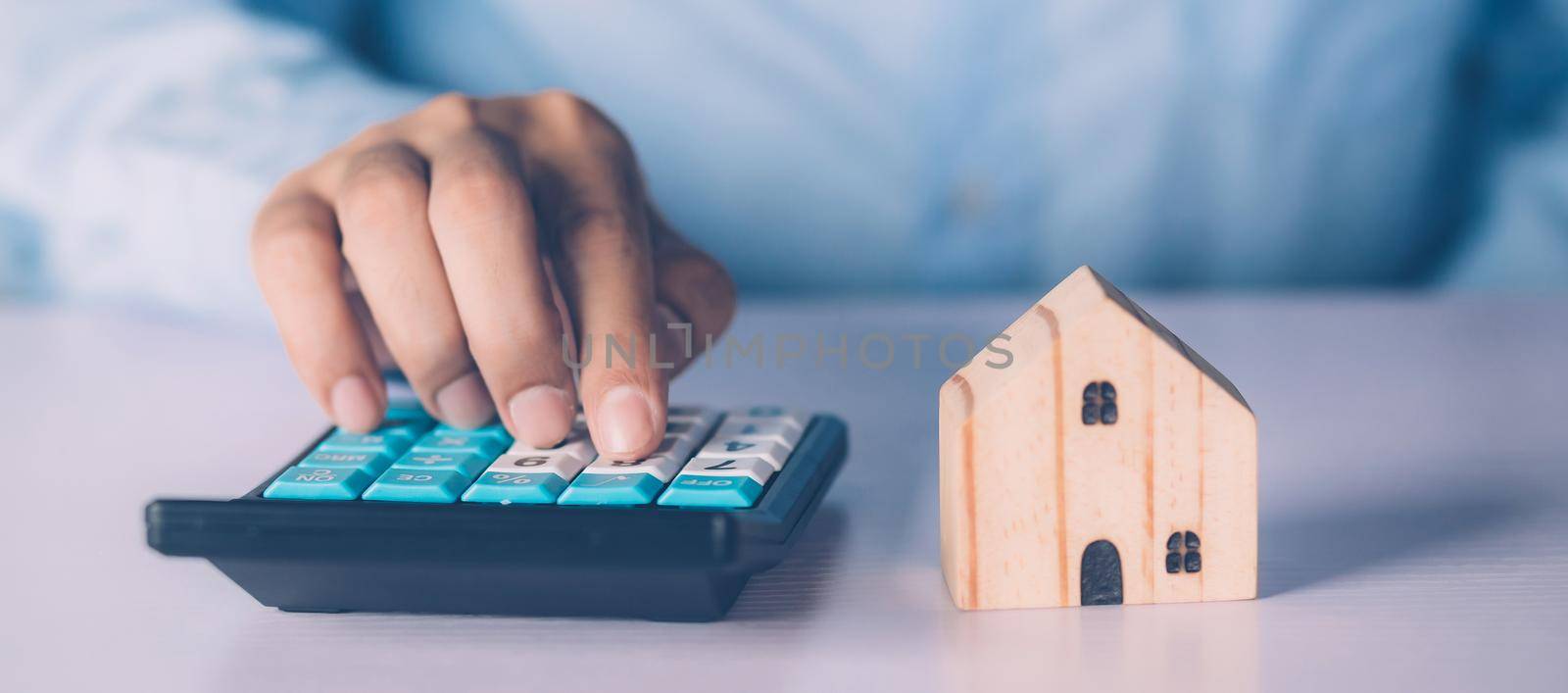 Hand of businessman planning and calculate expense and mortgage with calculator and home on desk, insurance and budget of residential, examining of loan and residence, business and property concept.