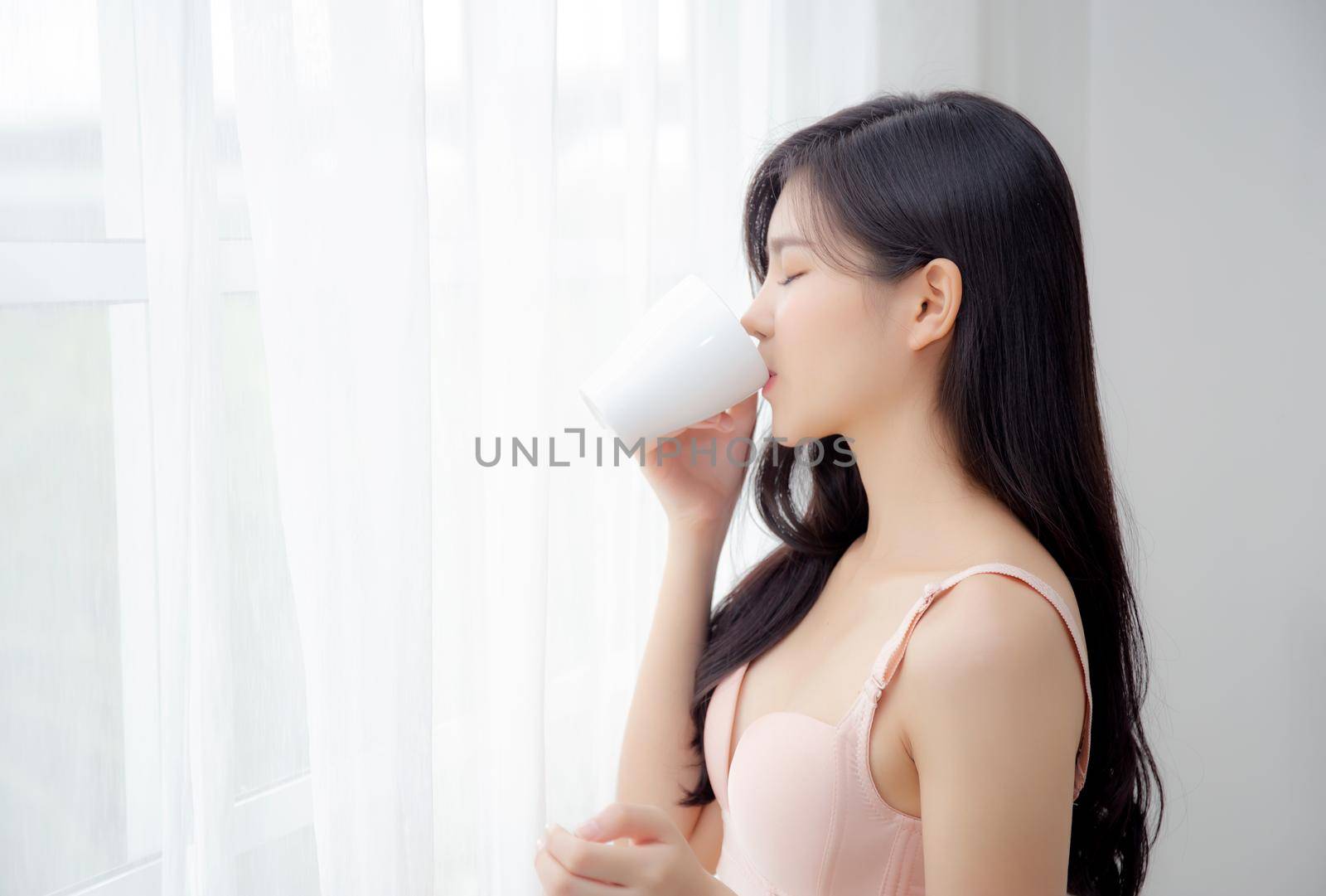 Beautiful young asian sexy woman in underwear drinking coffee near windows in the morning, girl with seductive figure fit drinking beverage for relax and resting after wake up, lifestyle concept.