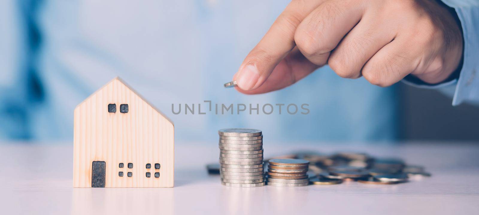 Hand of business man holding stack of coins and model home, wealth with finance and saving for residence and success, loan and mortgage for residential, investment for real estate, property concept.
