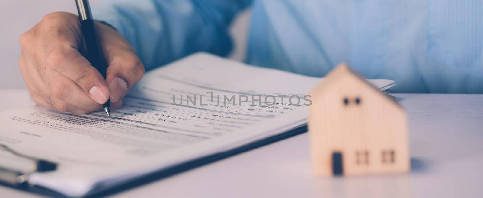 Real estate agent holding home and signing contract about agreement of real property on desk, house broker and planning investment, businessman writing on document form rent house, business concept. by nnudoo