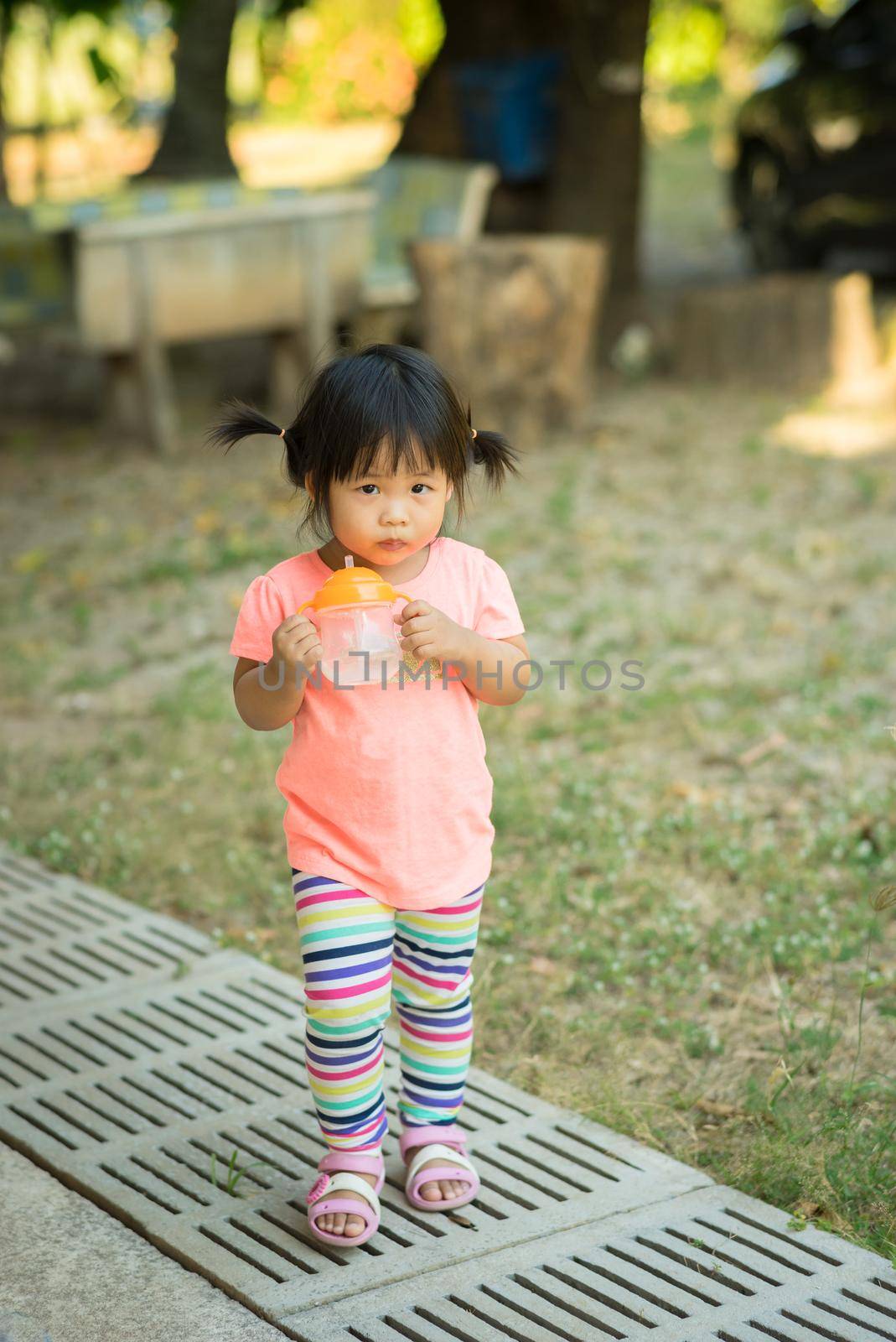 child girl hold drinking water bottle and runing in the park by domonite