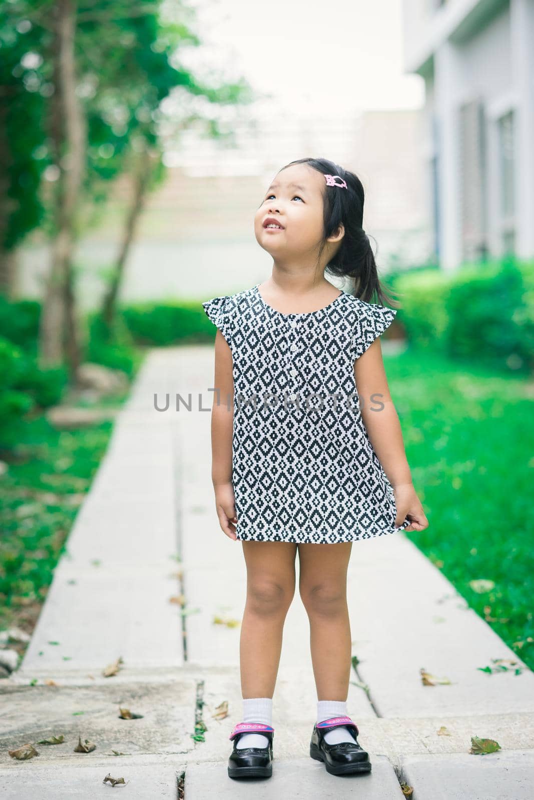 Portrait of happy asian little girl in dress standing on footpath in the park